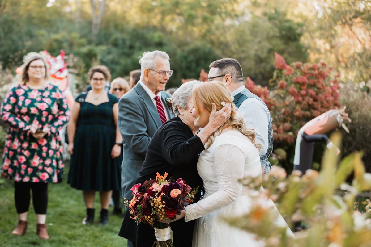 Wedding party gathers outdoors amidst autumn foliage and natural garden scenery.