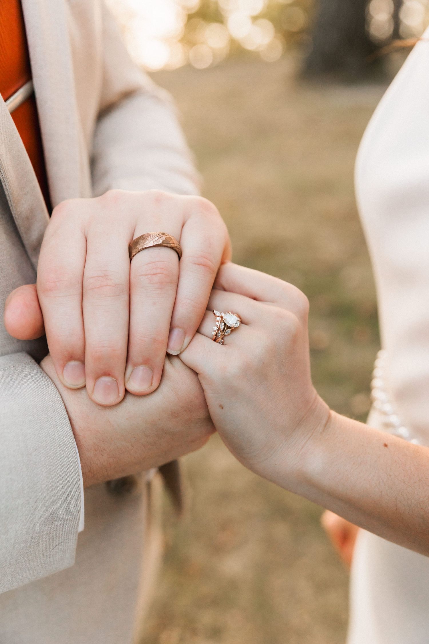 Close-up of hands holding each other with engagement ring sparkling in soft golden sunlight.