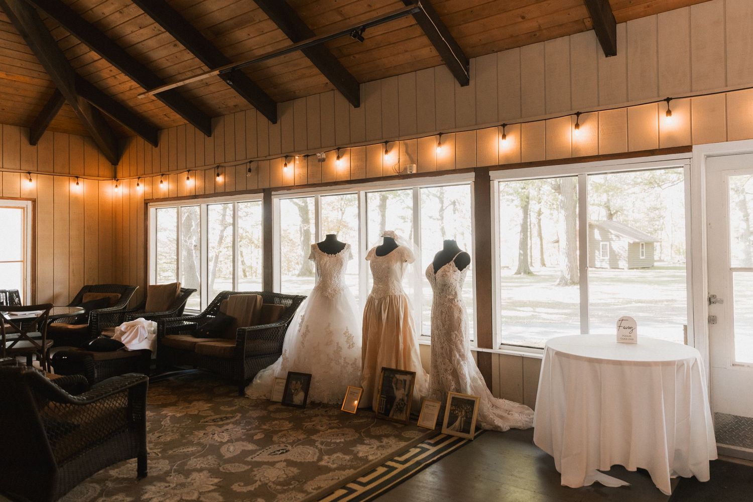 Wedding gowns on display in a cozy venue with wooden beams, string lights and natural lighting through windows.