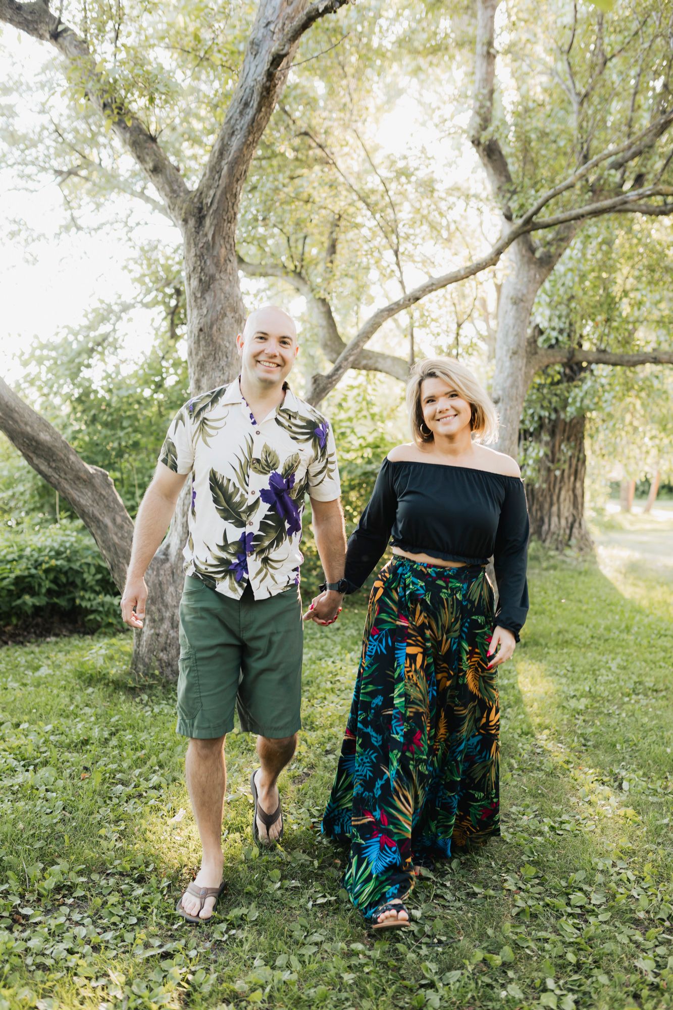 Couple posing together outdoors wearing coordinated casual outfits against a backdrop of trees.