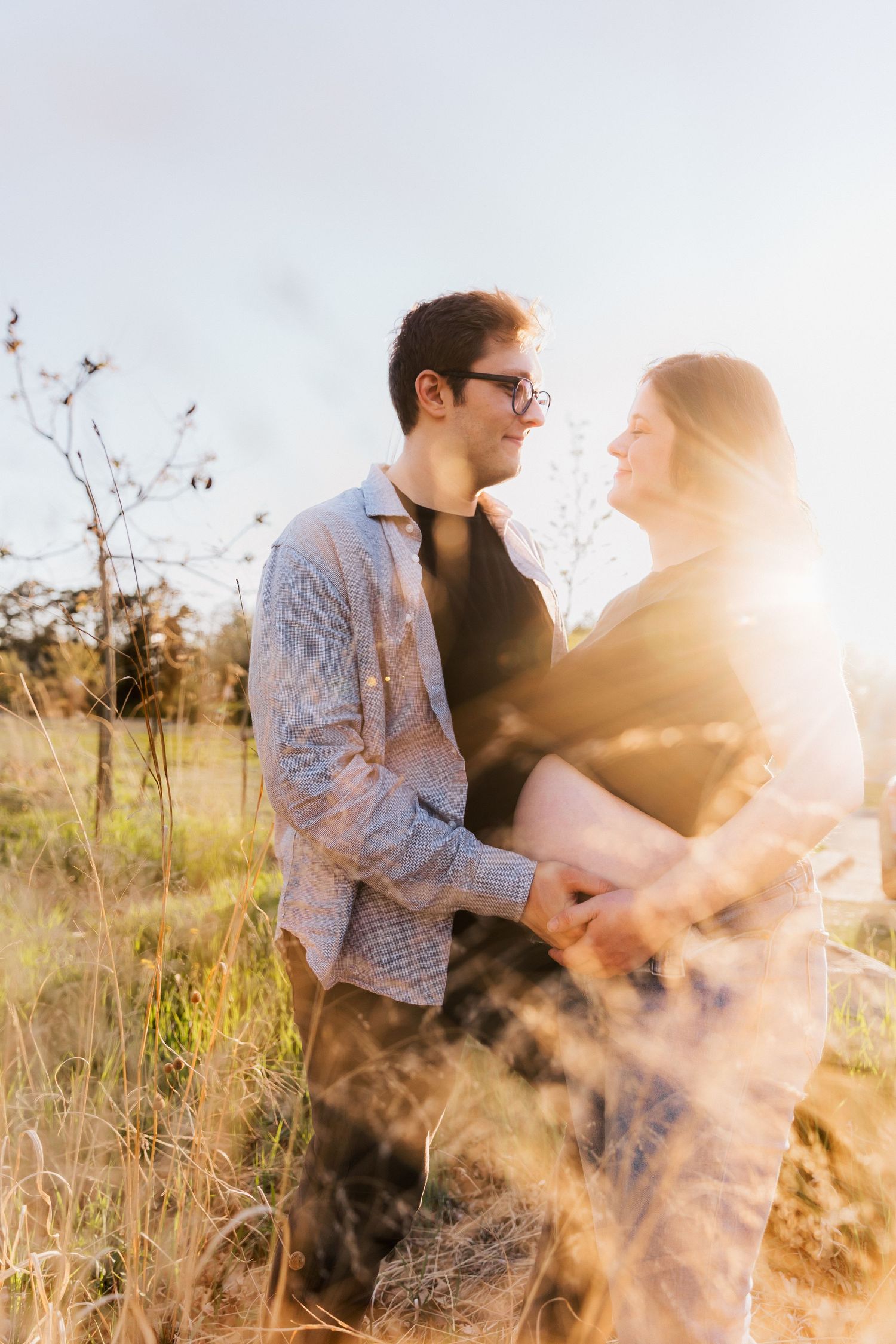 Couple embraces in sunlit field with tall grass.