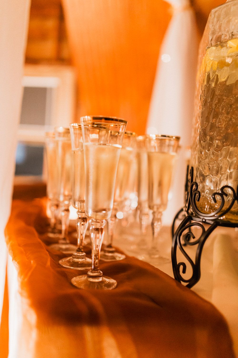 Elegant wine glasses and candle holders arranged on a table with warm orange ambient lighting create a romantic atmosphere.