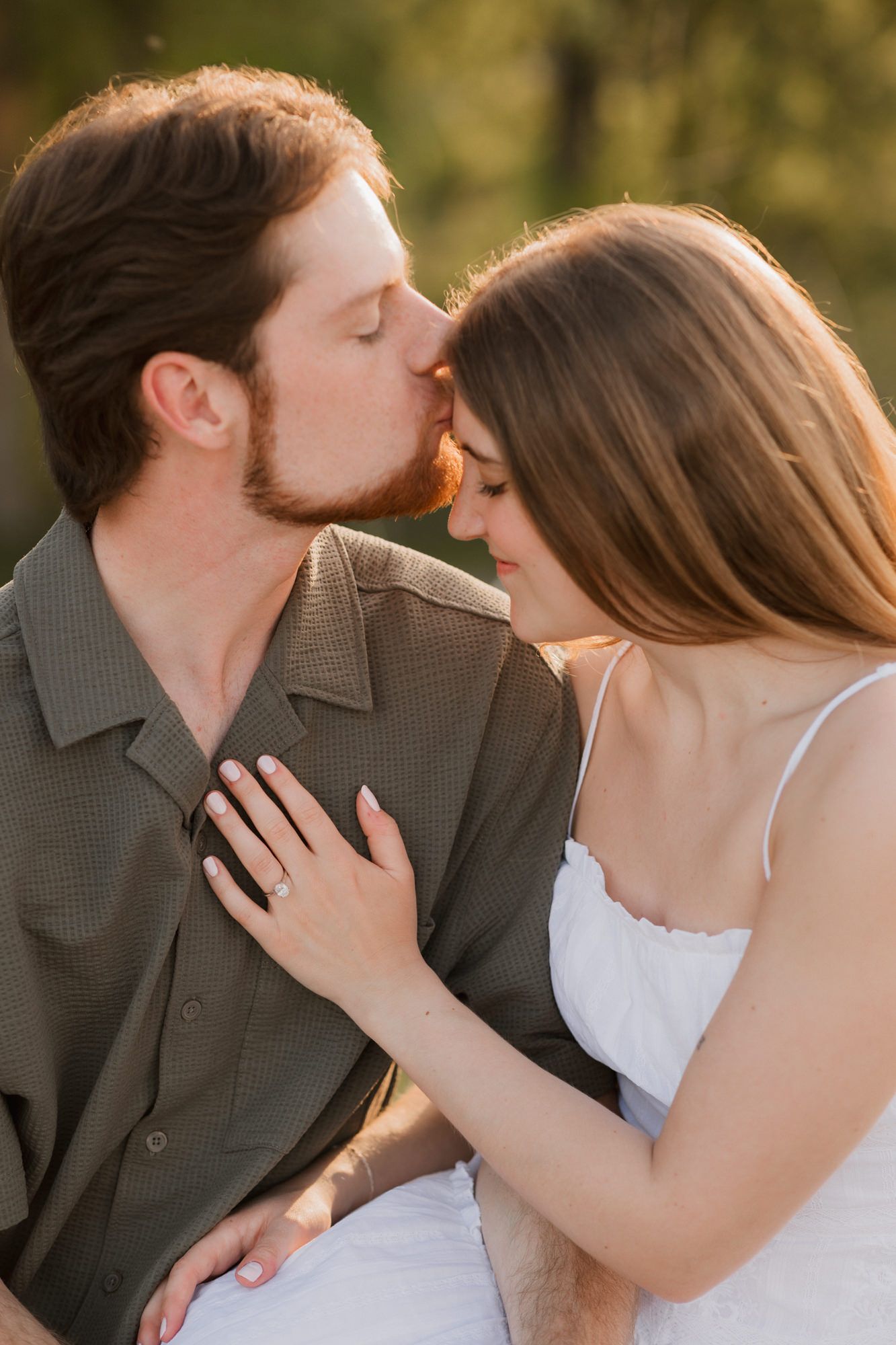 Man in olive shirt kisses womans forehead as she places hand on his chest outdoors.