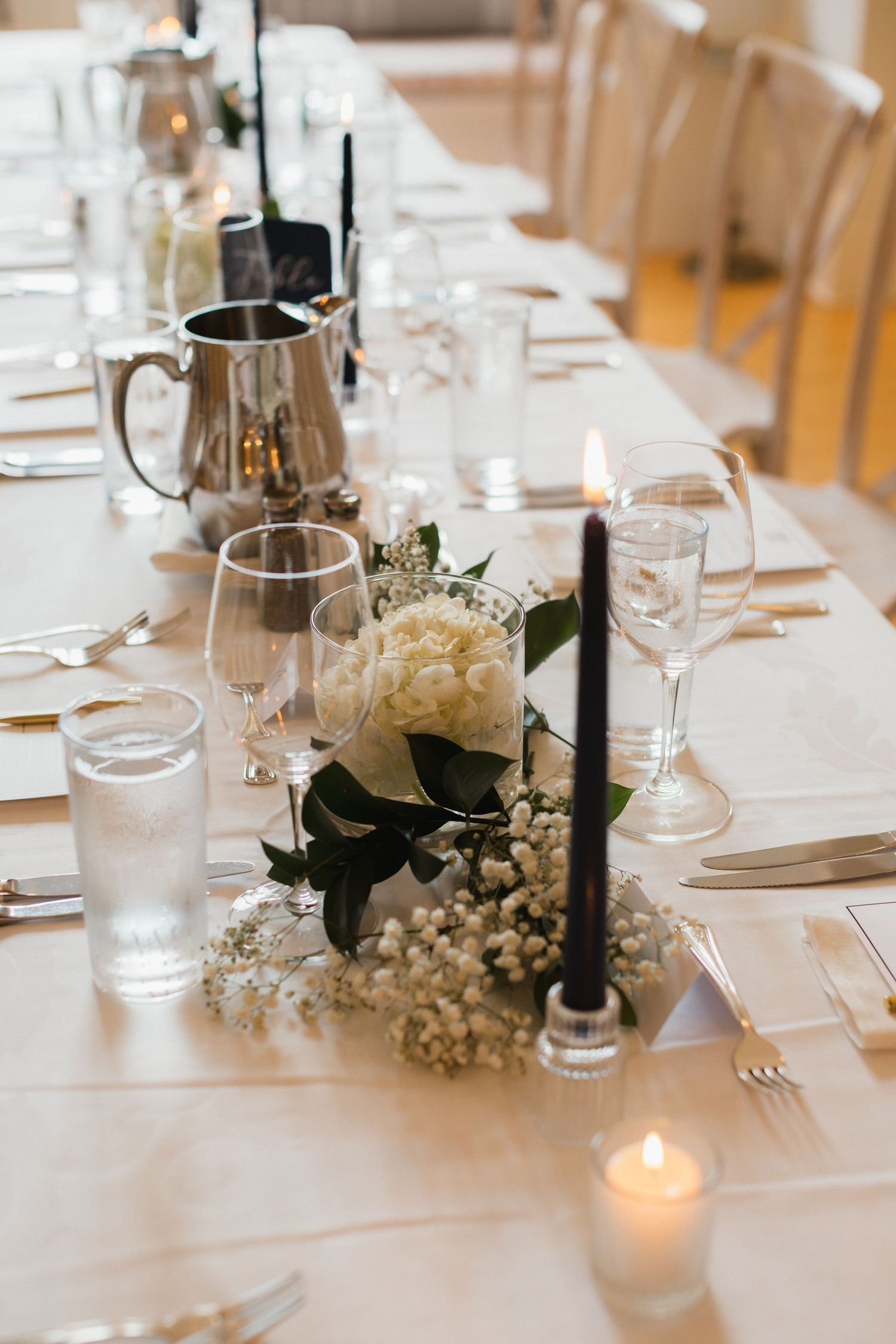 Elegant wedding reception table set with white floral centerpieces, black taper candles, and glassware.