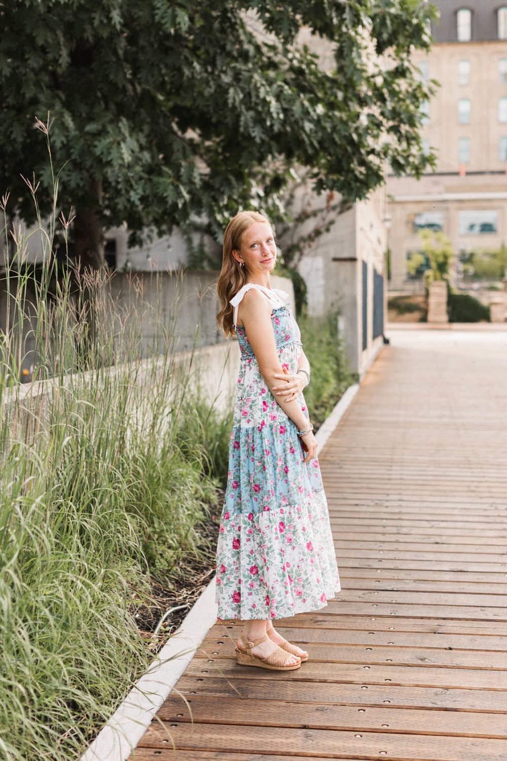 Floral maxi dress styled photo on a wooden boardwalk with ornamental grasses and urban architecture.