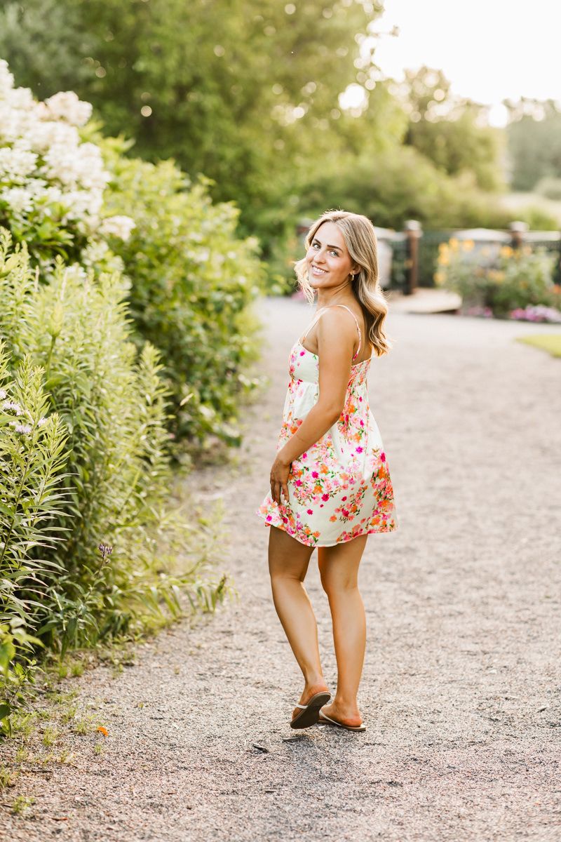 Summer portrait of a person in a floral sundress posing on a garden path surrounded by lush greenery.