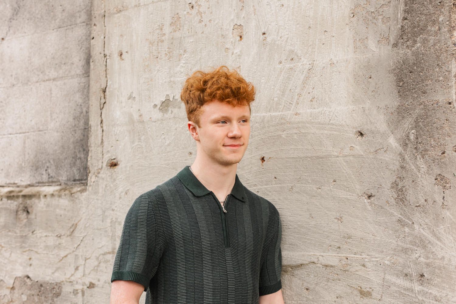 A person in casual attire leans casually against a gray concrete wall background.