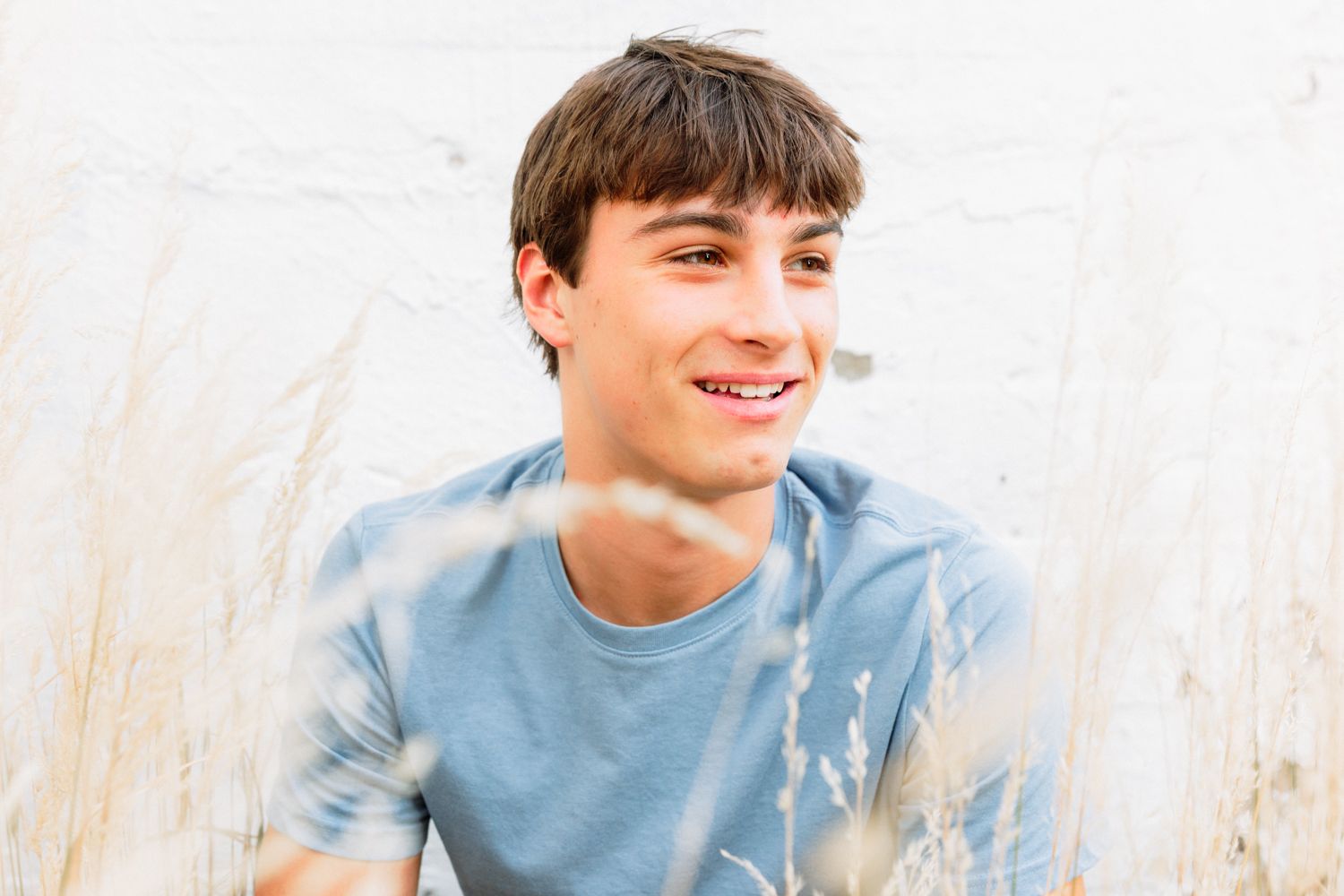 Candid outdoor portrait with white wall background and natural lighting.
