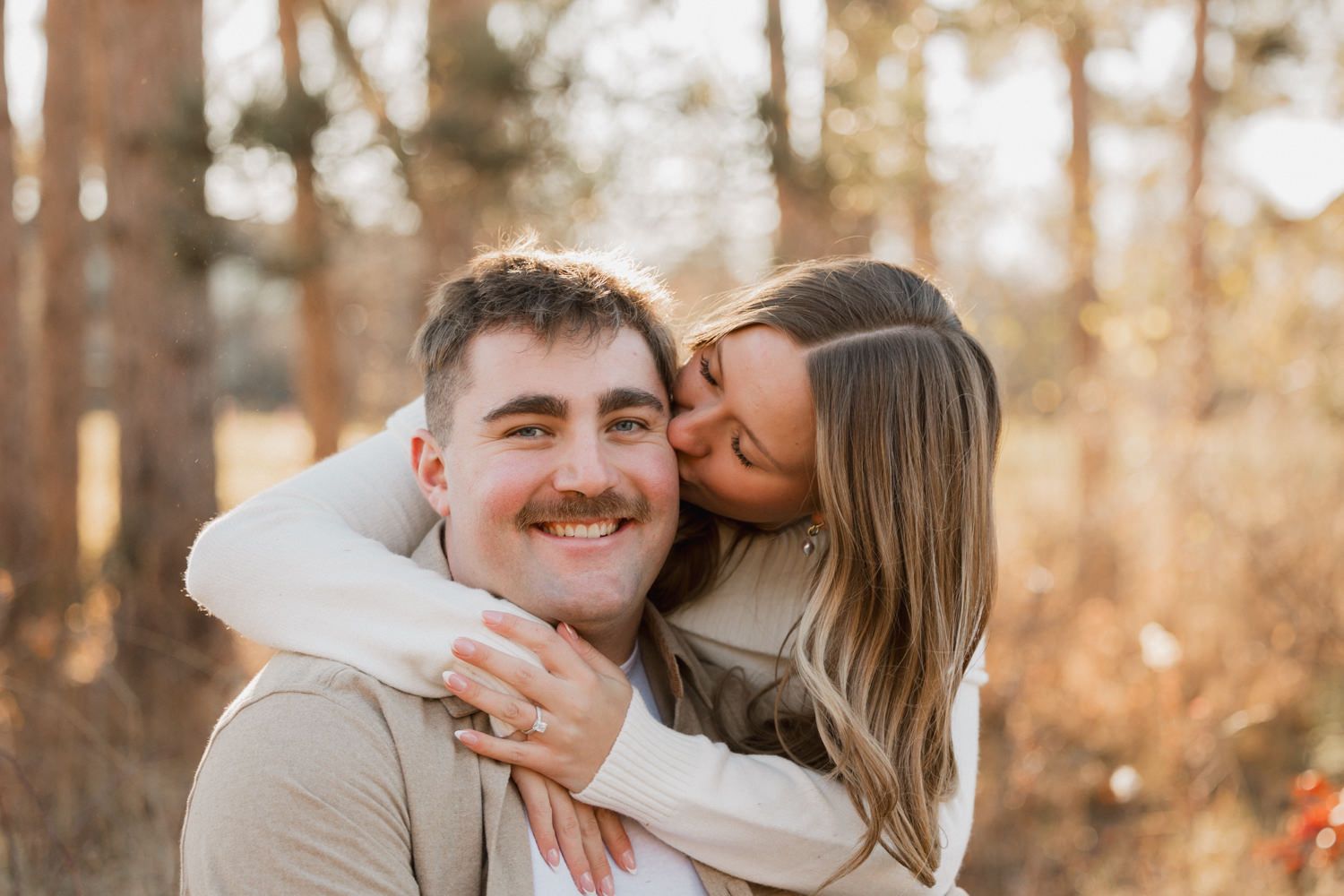 A tender embrace captured in warm sunlight as a couple shares an affectionate moment in a wooded setting.