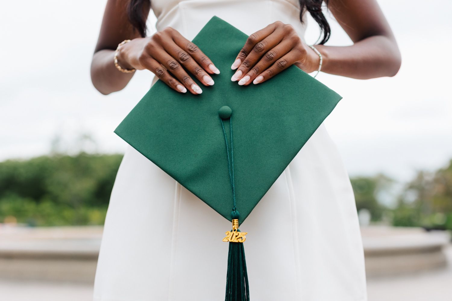 Graduate in white dress posing with green graduation cap.