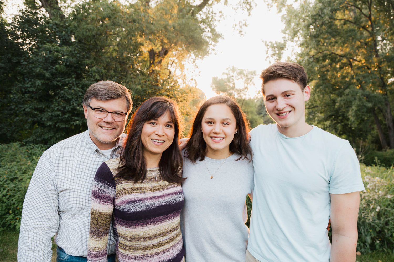Four people smile warmly at the camera during an outdoor photo session at sunset.