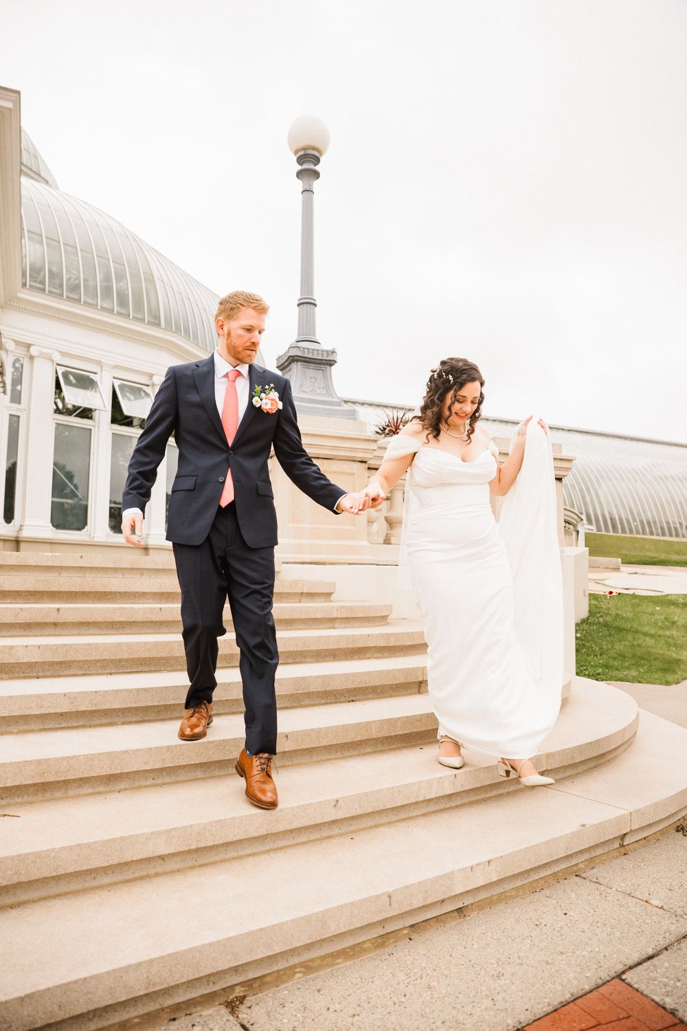 Couple descending stone steps outside a conservatory building in a romantic wedding moment.