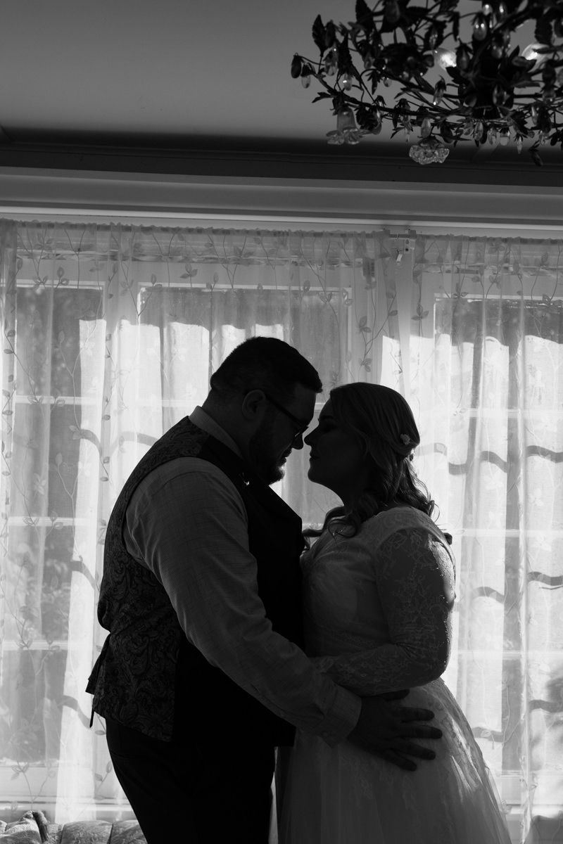 A romantic black and white silhouette of a couple embracing by a lace-curtained window.