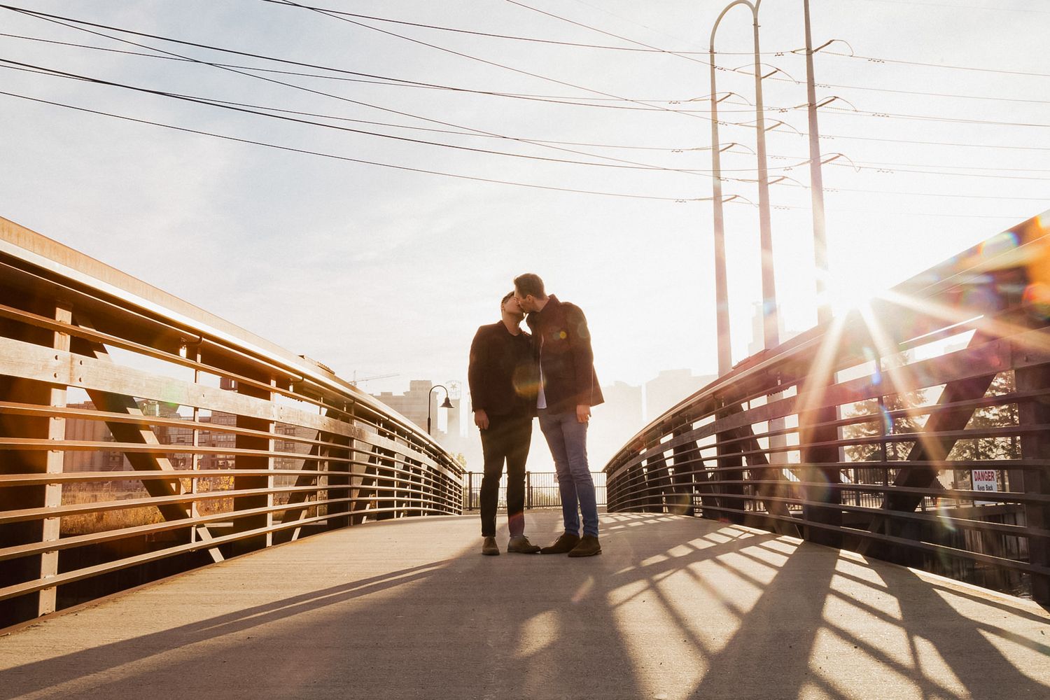 Couple sharing a romantic moment on a bridge at golden hour with sun flare.
