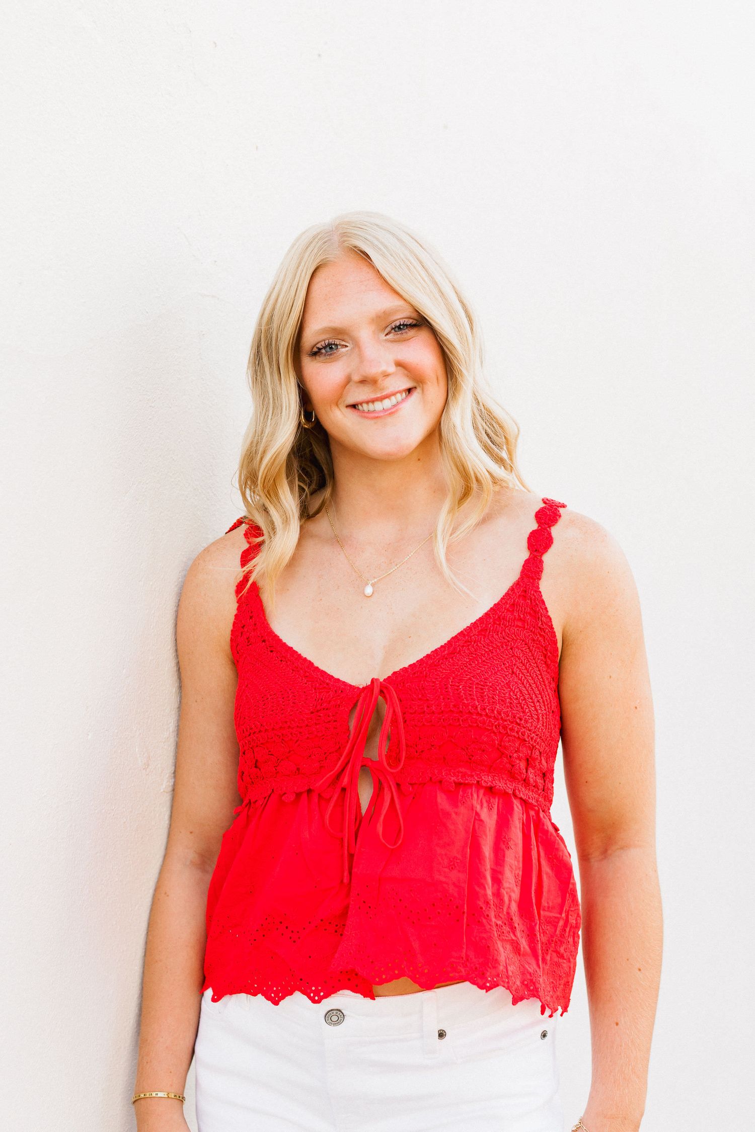 A bright red sleeveless blouse with scalloped details is showcased against a clean white background.