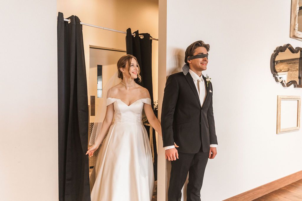 A couple in wedding attire stands beside a doorway during their first look moment.
