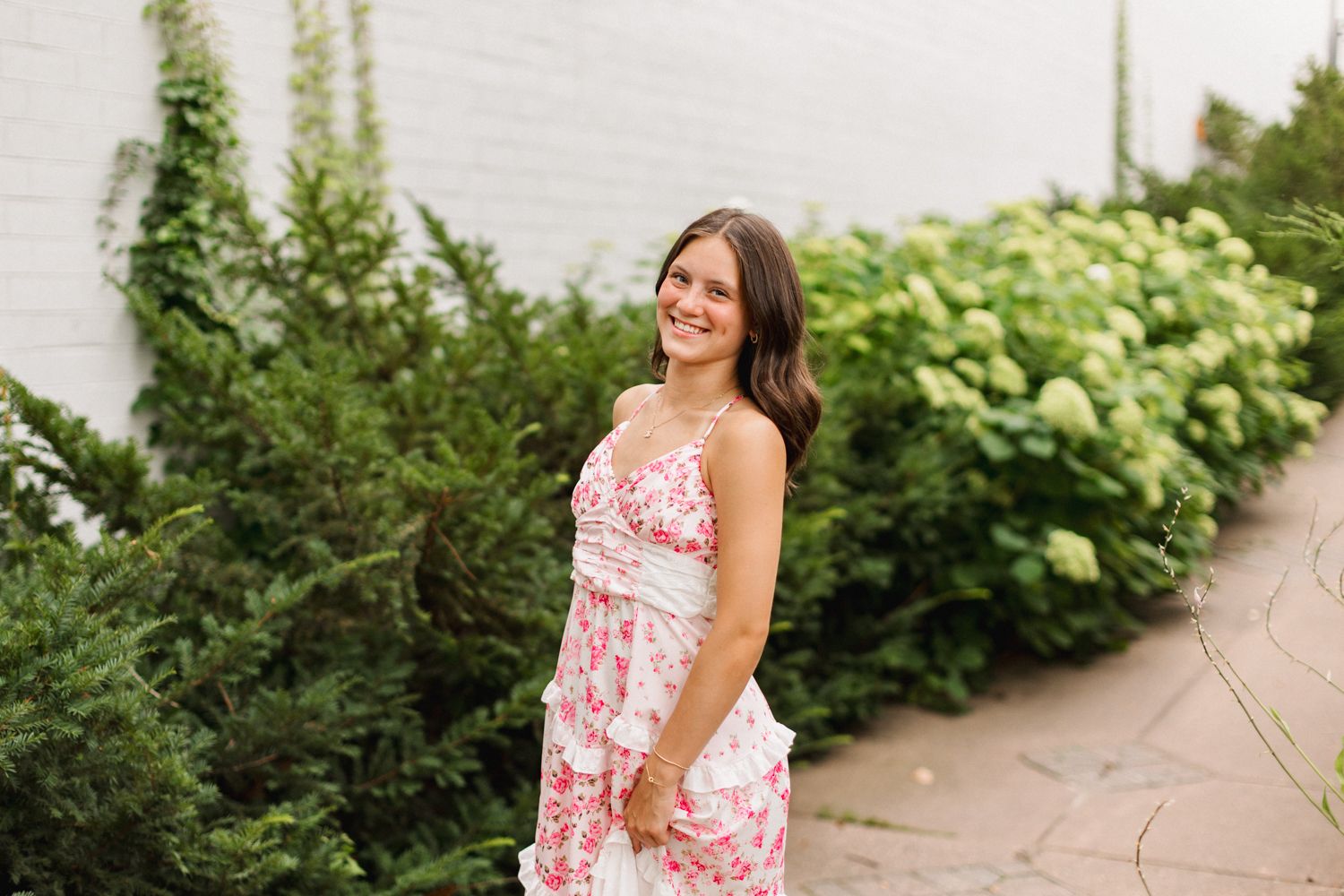 Woman wearing a summer floral dress stands against a backdrop of lush green foliage.
