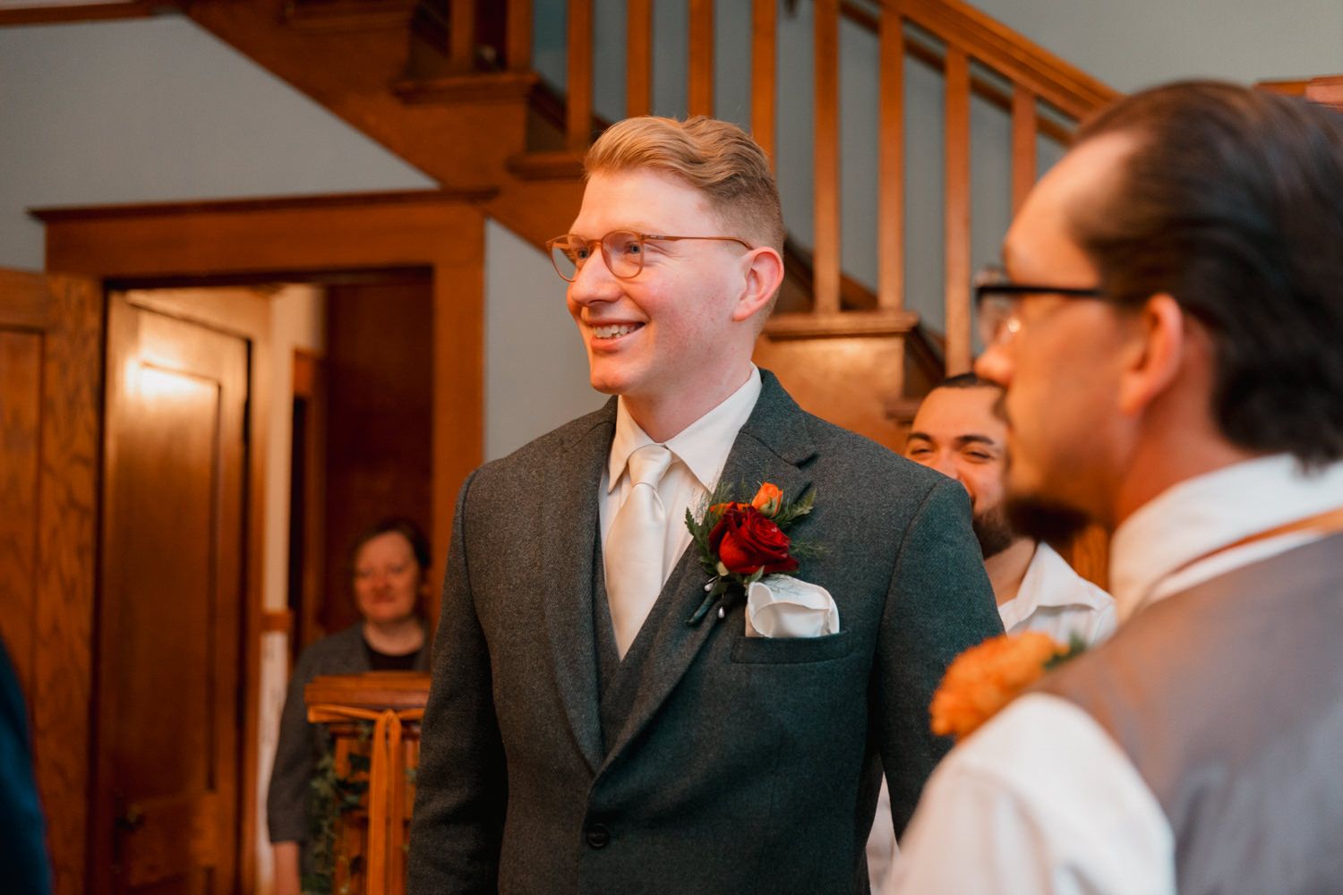 Wedding guests mingle in a wood-paneled room with warm lighting and formal attire.