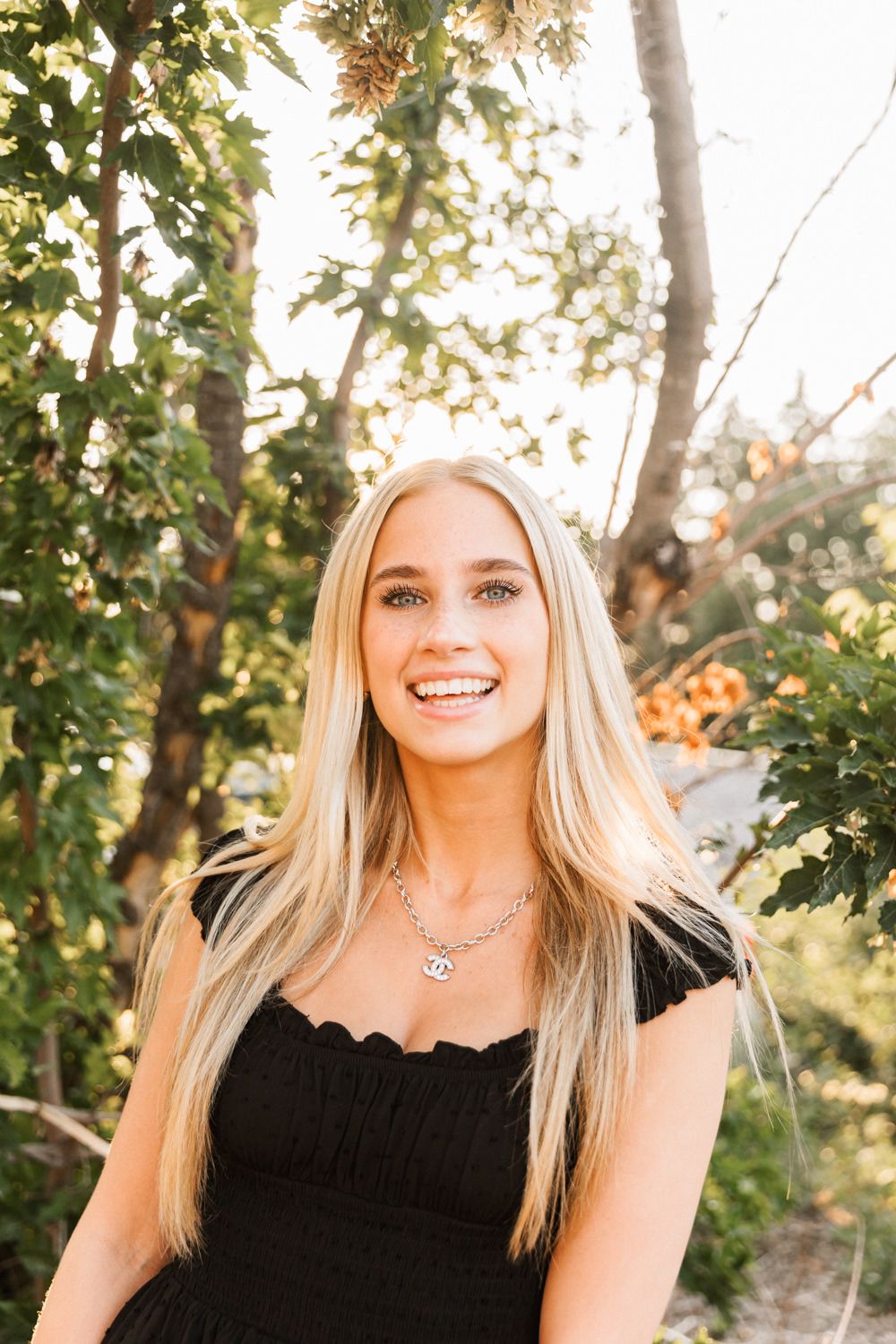 Natural outdoor portrait with sunlit trees and black summer dress.