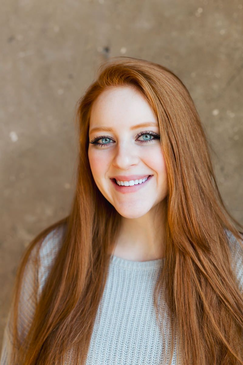 Close-up portrait of person with long red hair wearing light sweater against neutral background.