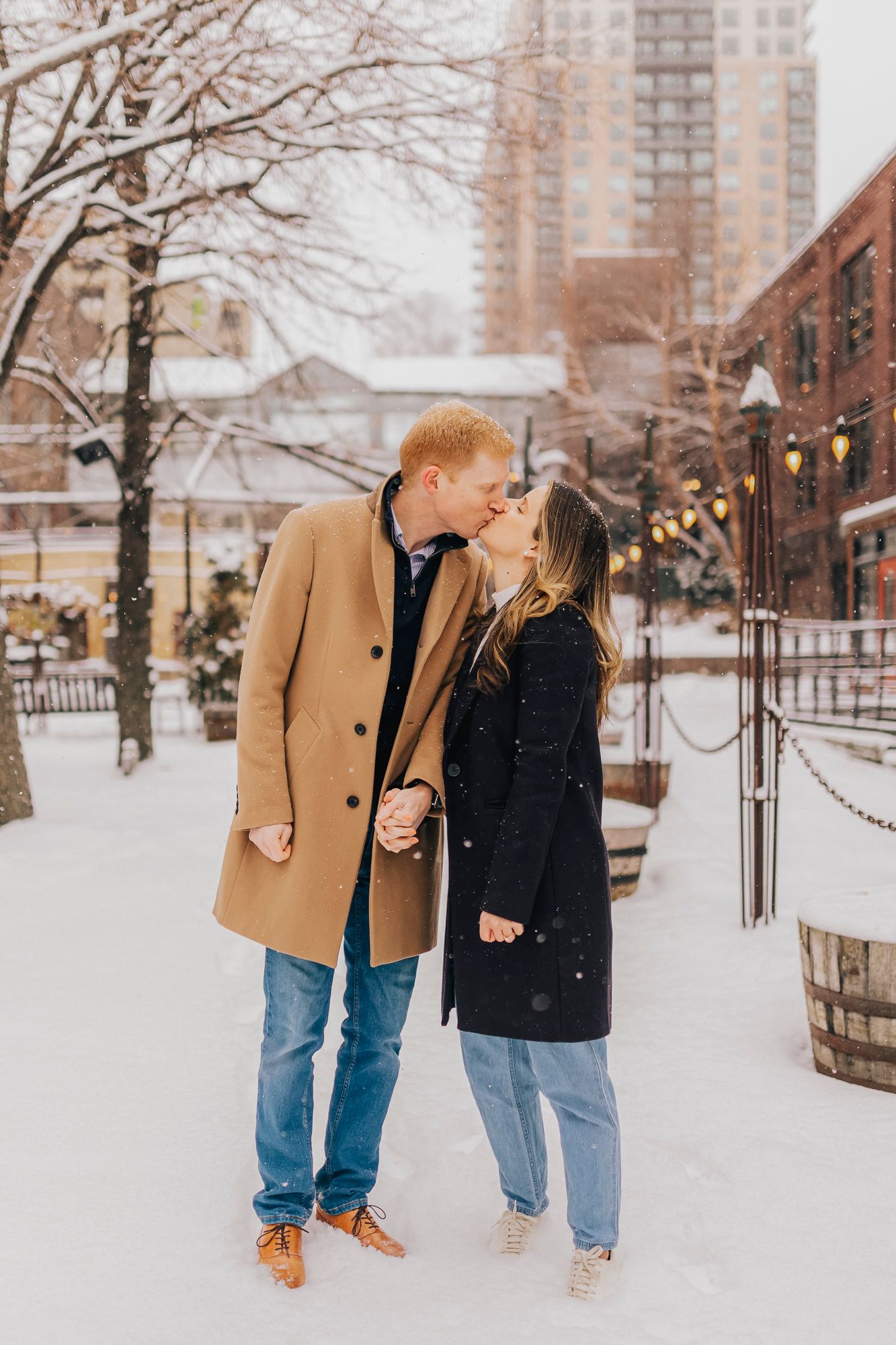 A winter urban engagement photo with city buildings and snow-covered trees in the background.