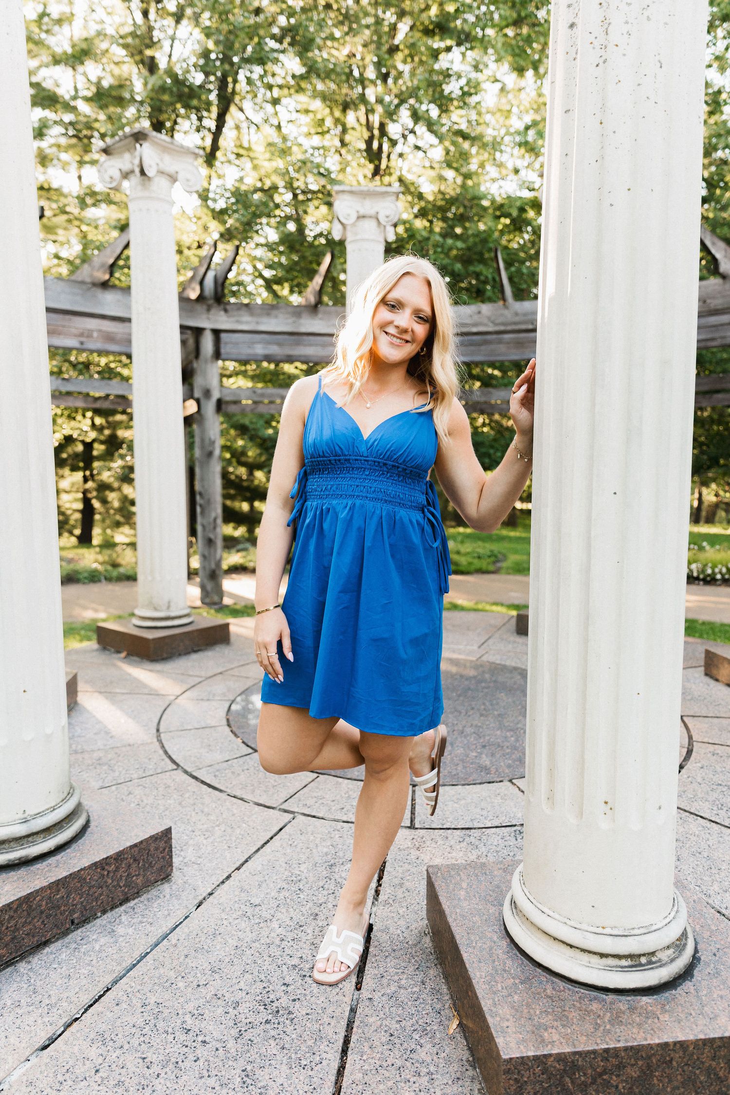 A bright blue summer dress stands out against white columns in an outdoor portrait setting.