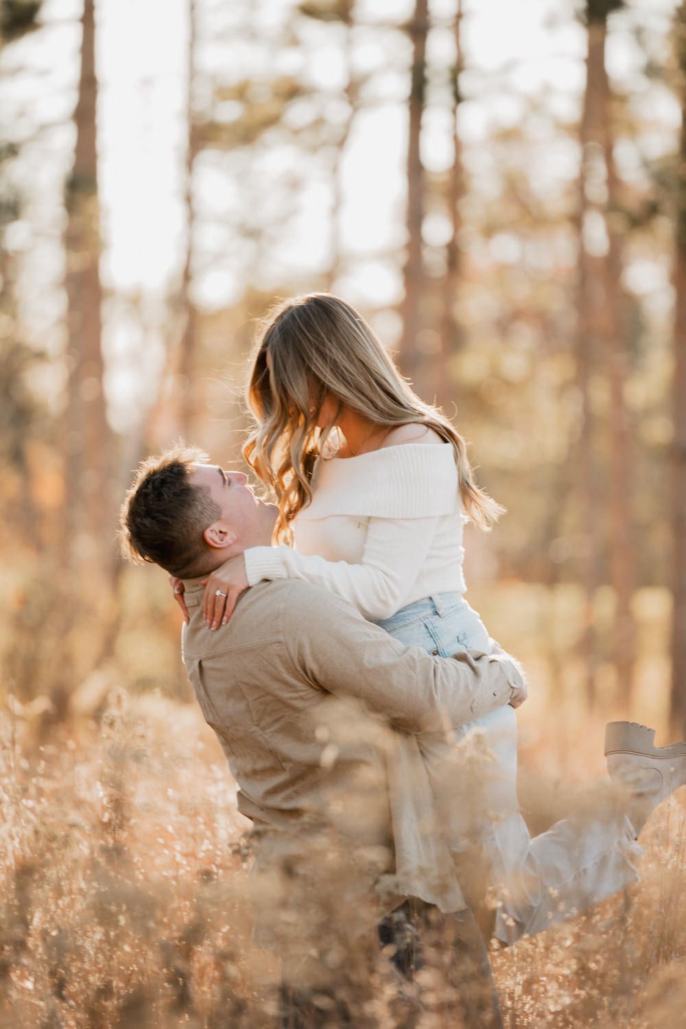 A romantic couple embraces in a sunlit autumn field with tall grass and trees in the background.