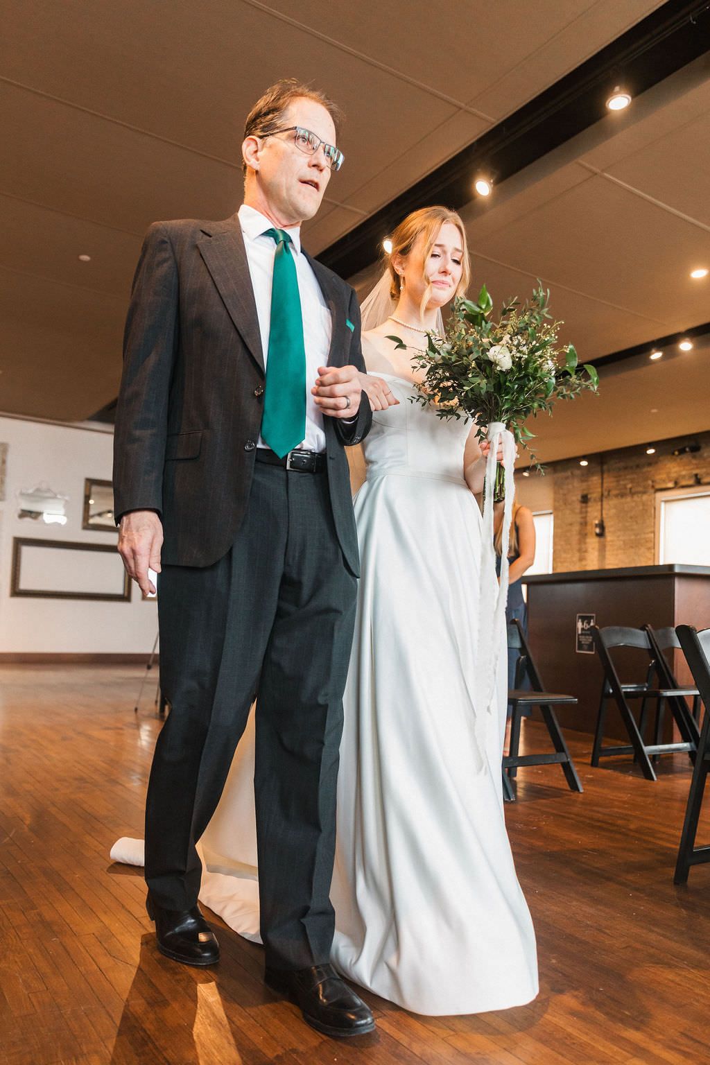 Couple walks arm in arm during wedding ceremony in elegant venue with hardwood floors.