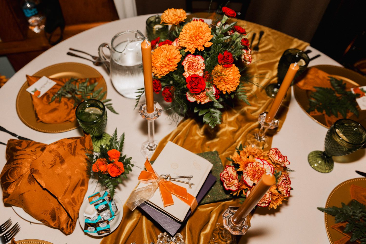 Wedding reception table decorated with orange and red flowers, candles, and place settings.