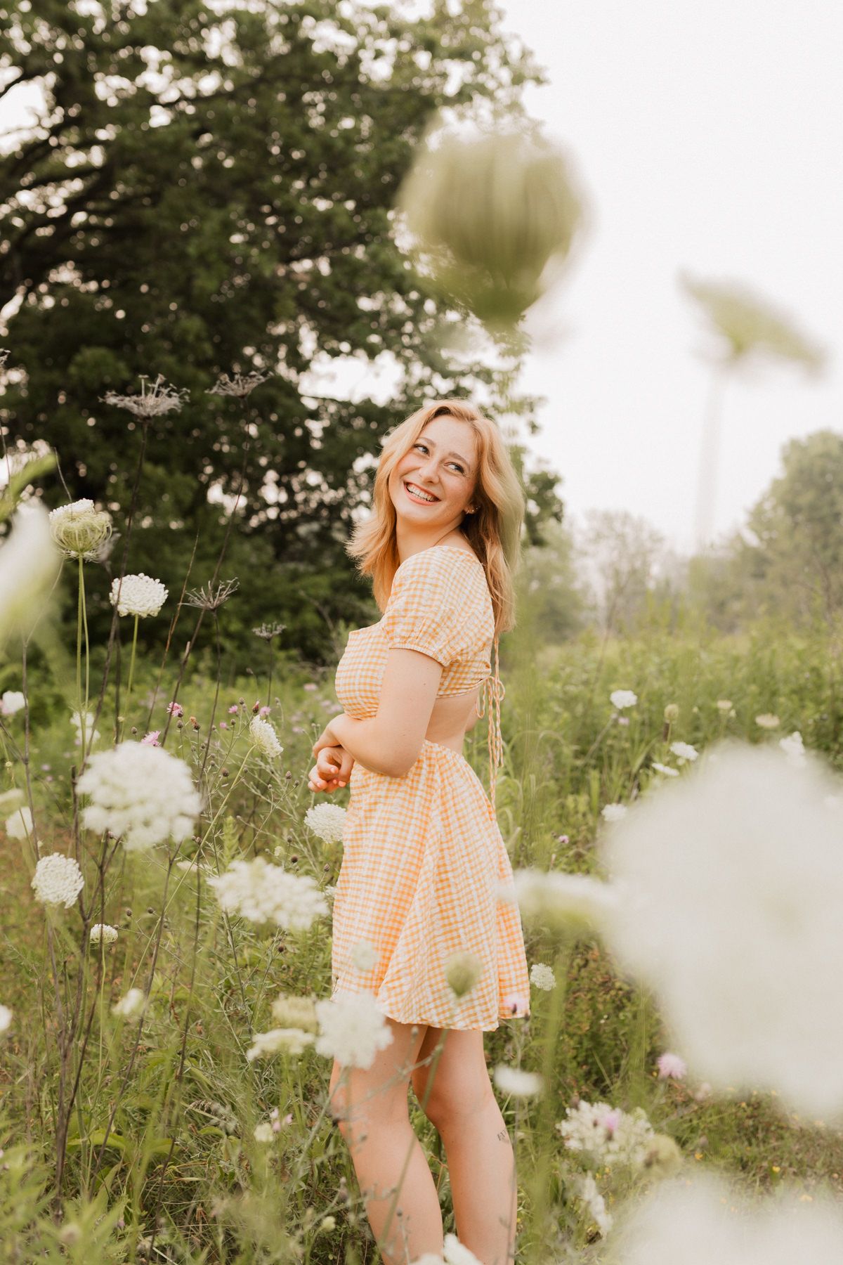 Cheerful young woman in yellow gingham dress smiling in a wildflower field.