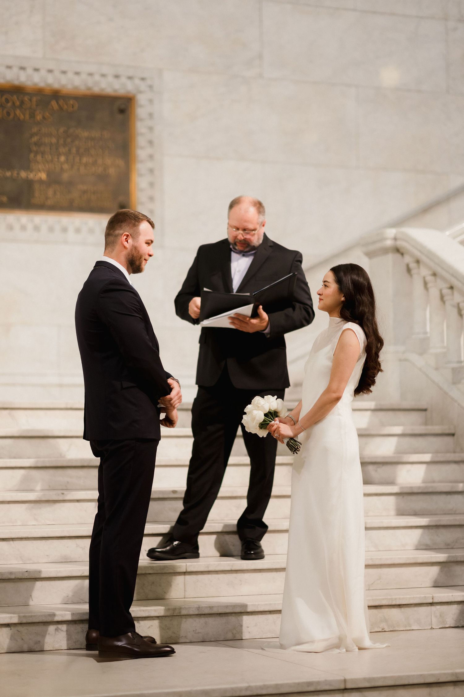 Couple exchanges vows on marble steps with officiant during elegant wedding ceremony.
