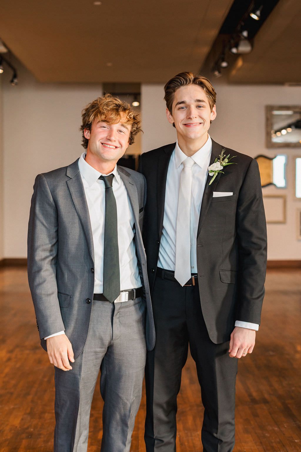 Line of groomsmen in matching gray and black suits smiling in an indoor venue.