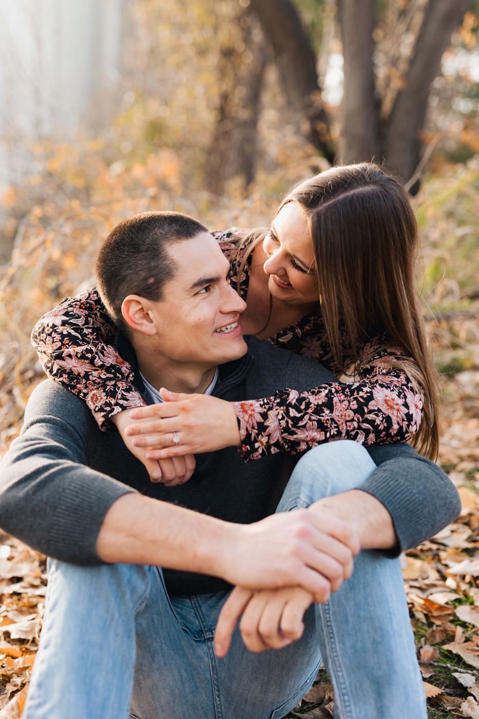 Couple sharing an intimate embrace while sitting on autumn leaves in a park.