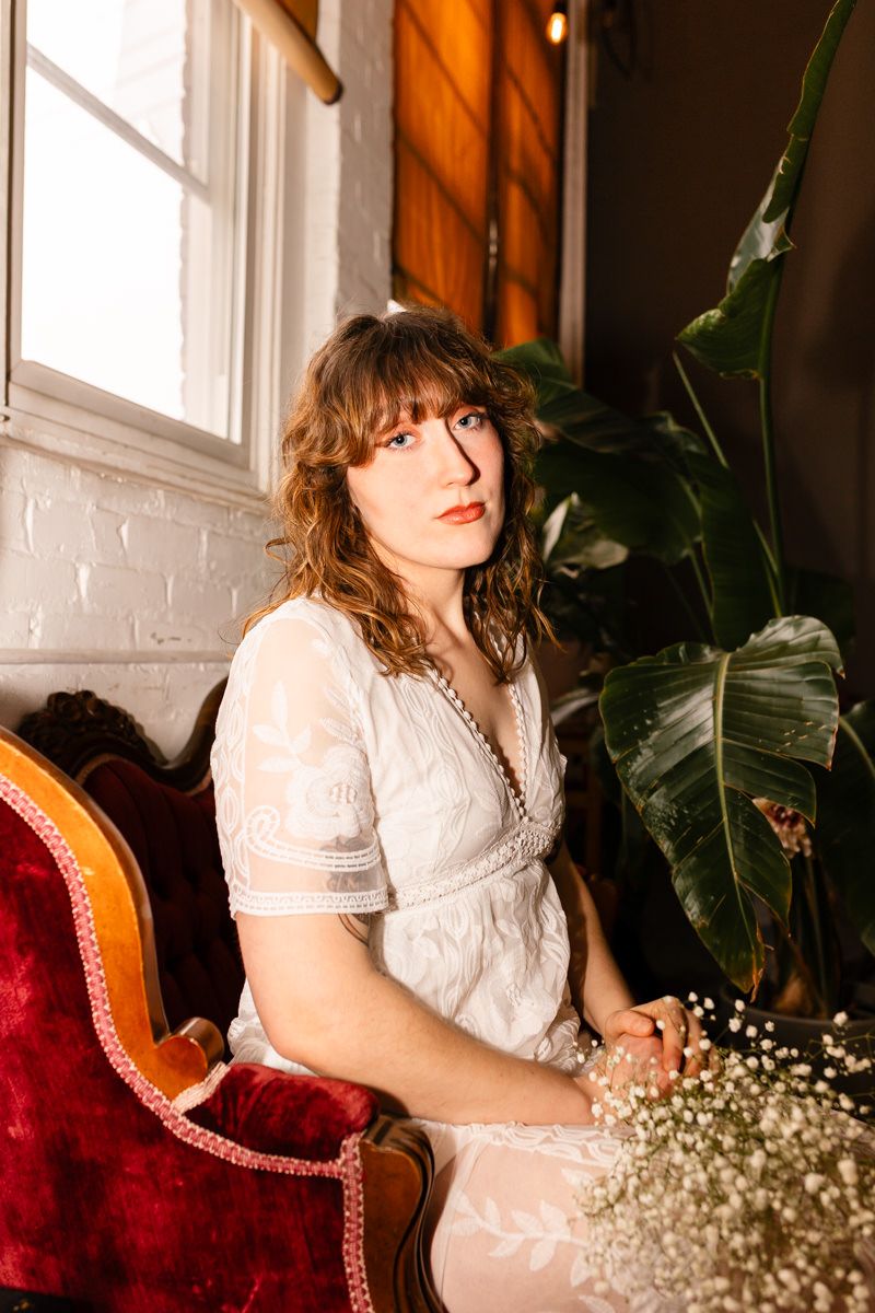 Interior portrait on a red velvet chair with baby's breath flowers and natural window light.