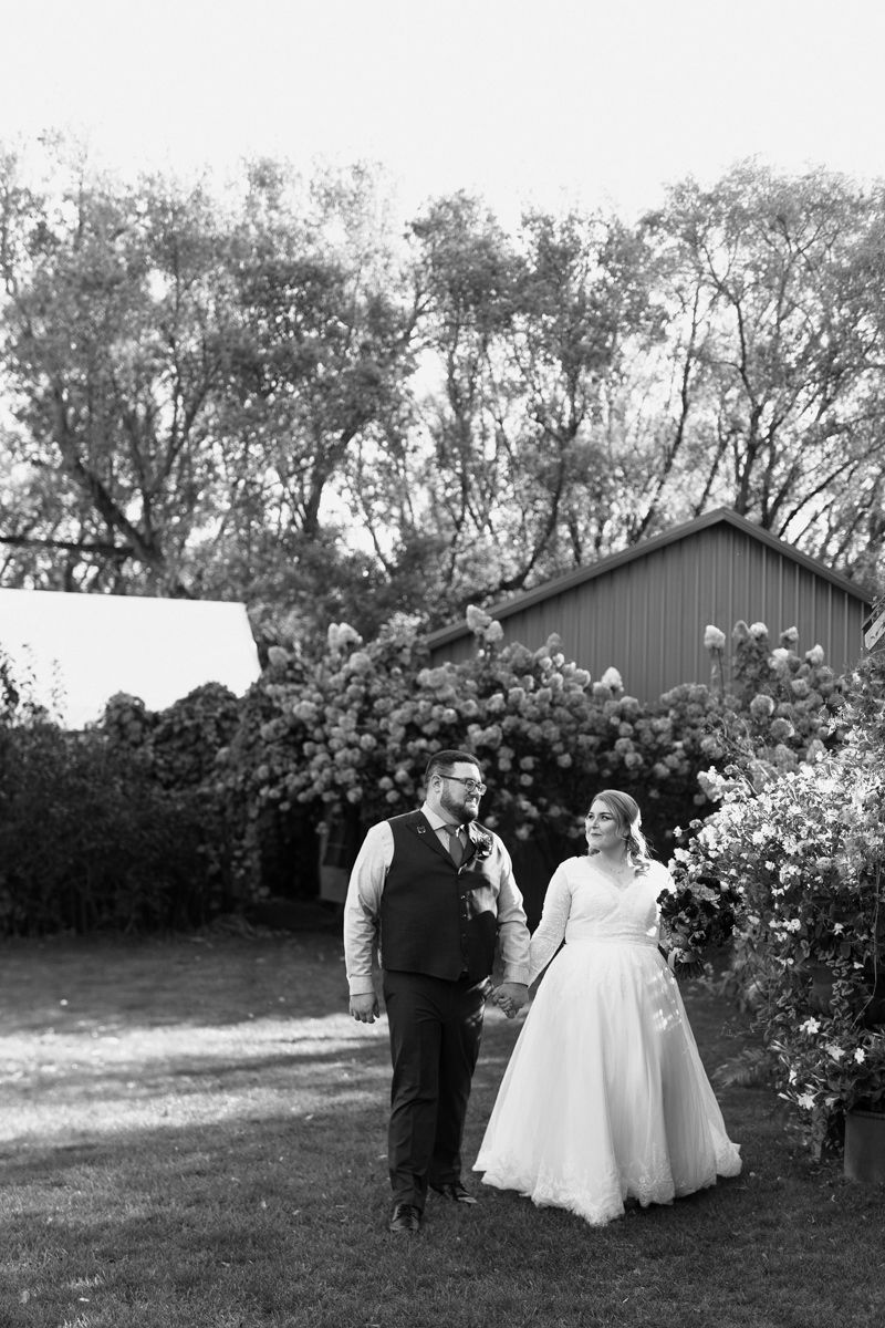 A romantic wedding scene with couples walking through a lush garden with blooming roses and a rustic barn backdrop.