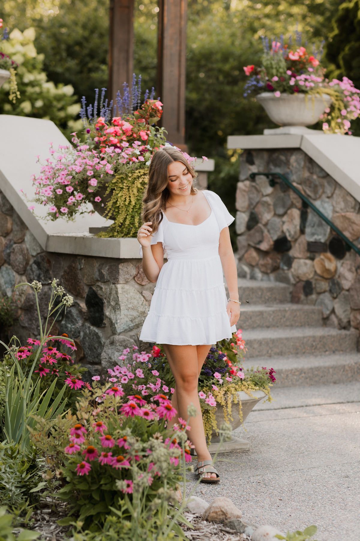Young woman in white mini dress strolling through vibrant garden with colorful blooming flowers.