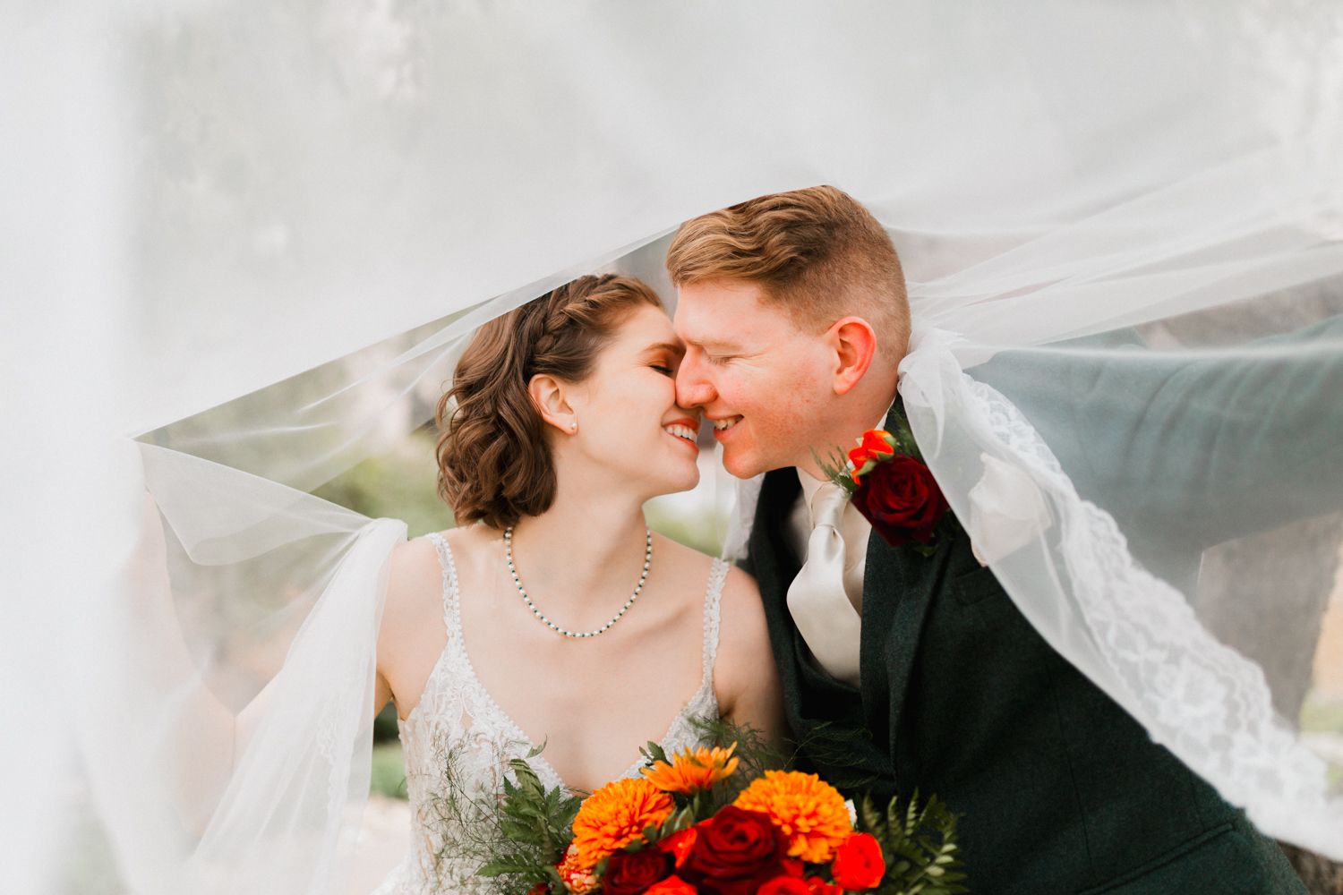 A romantic wedding couple shares a tender moment as the bride's veil flows dramatically in the wind.