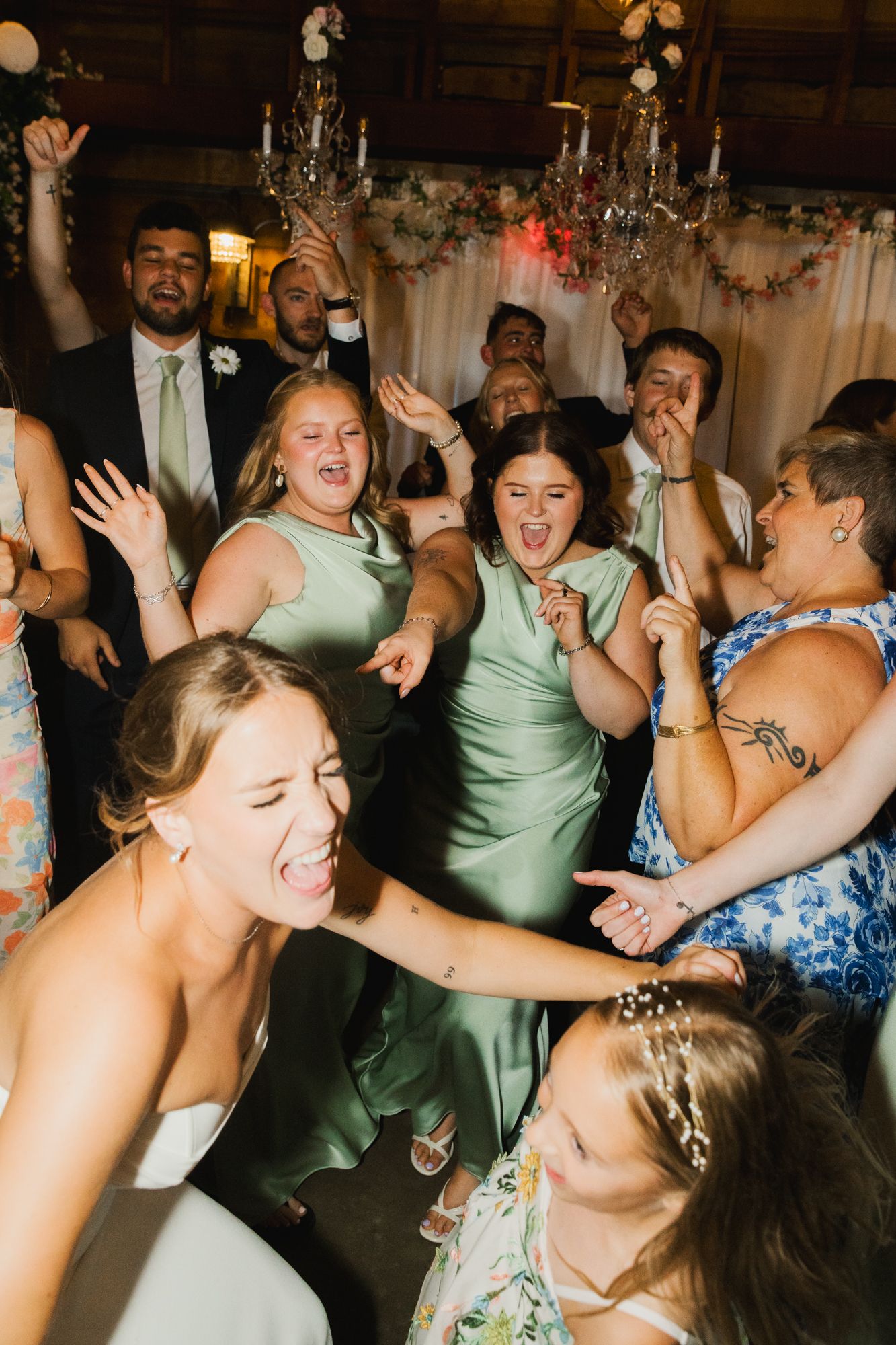 Joyful wedding guests and bridesmaids in sage green dresses dancing and celebrating at a lively wedding reception.