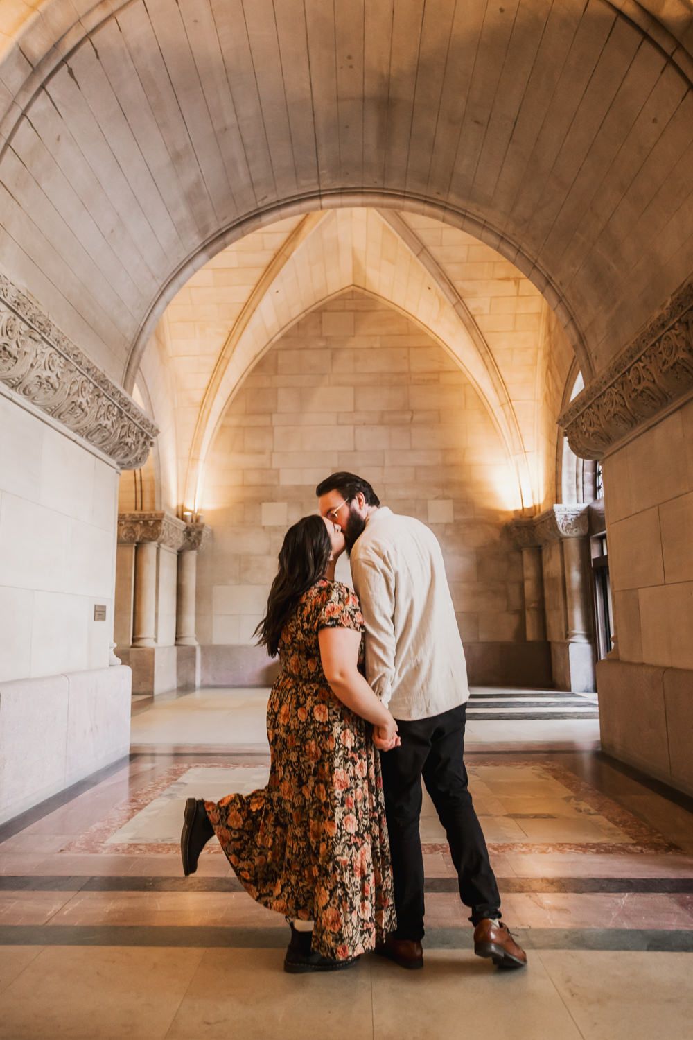 Romantic couple poses in arched stone hallway with dramatic lighting and architecture.
