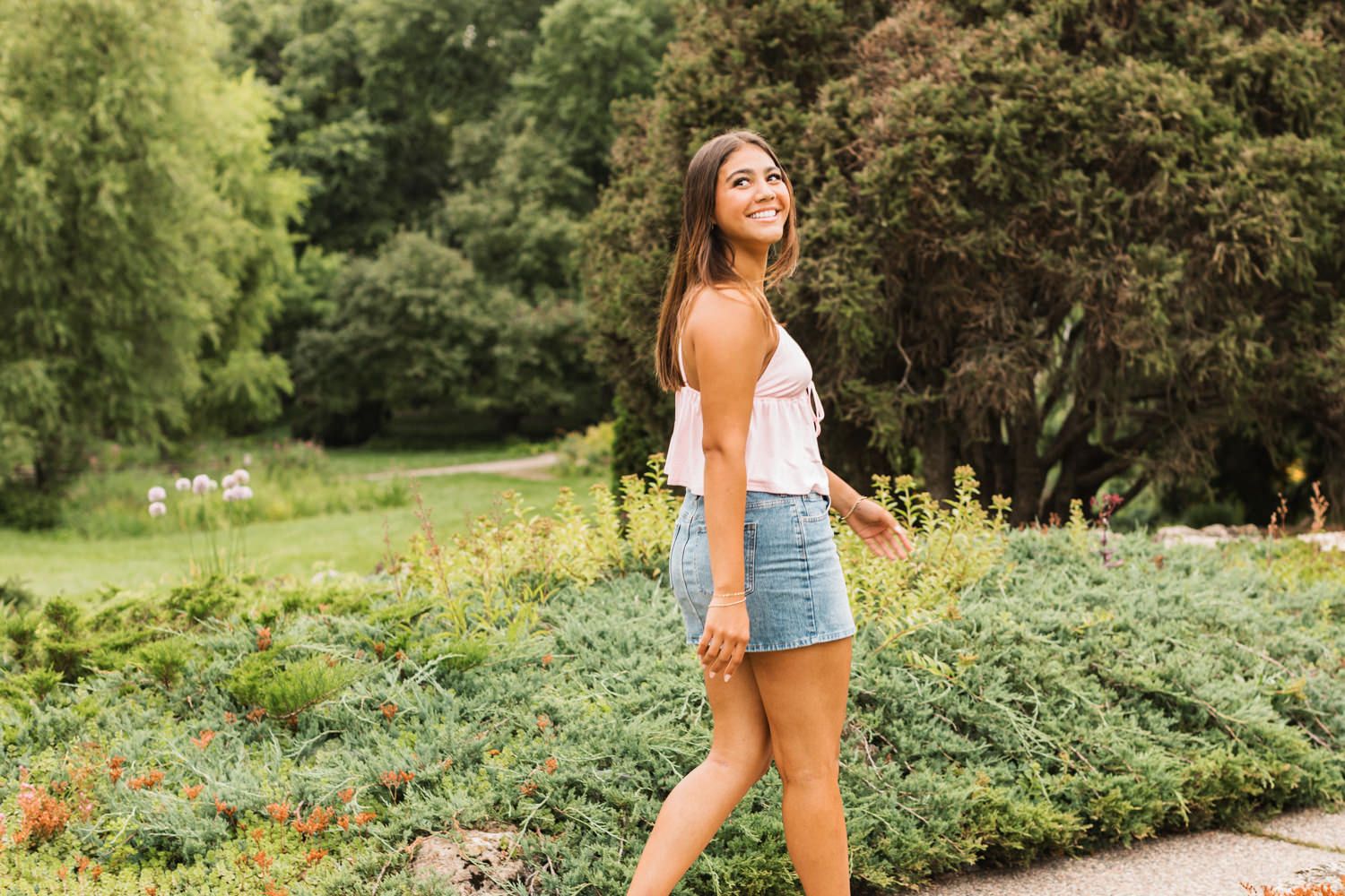 A woman laughs and dances joyfully among colorful wildflowers in a lush summer garden setting.