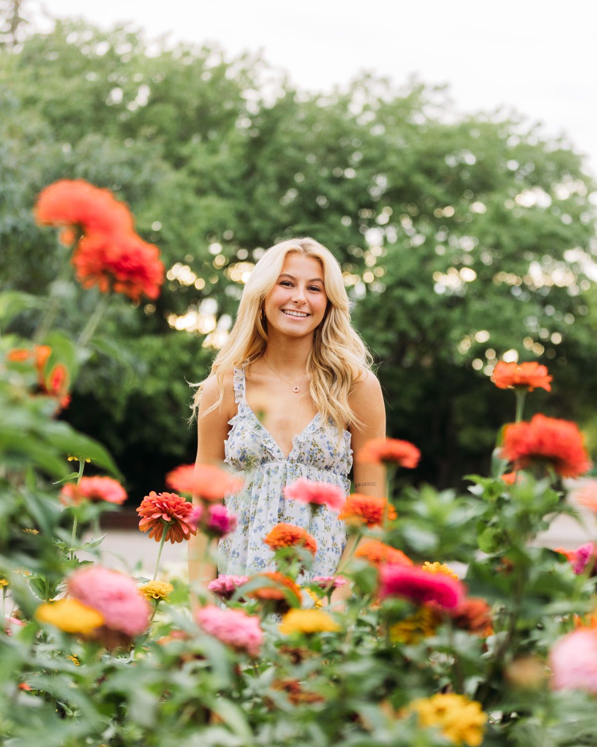 Woman in floral dress stands amidst colorful garden filled with vibrant orange and pink zinnias.
