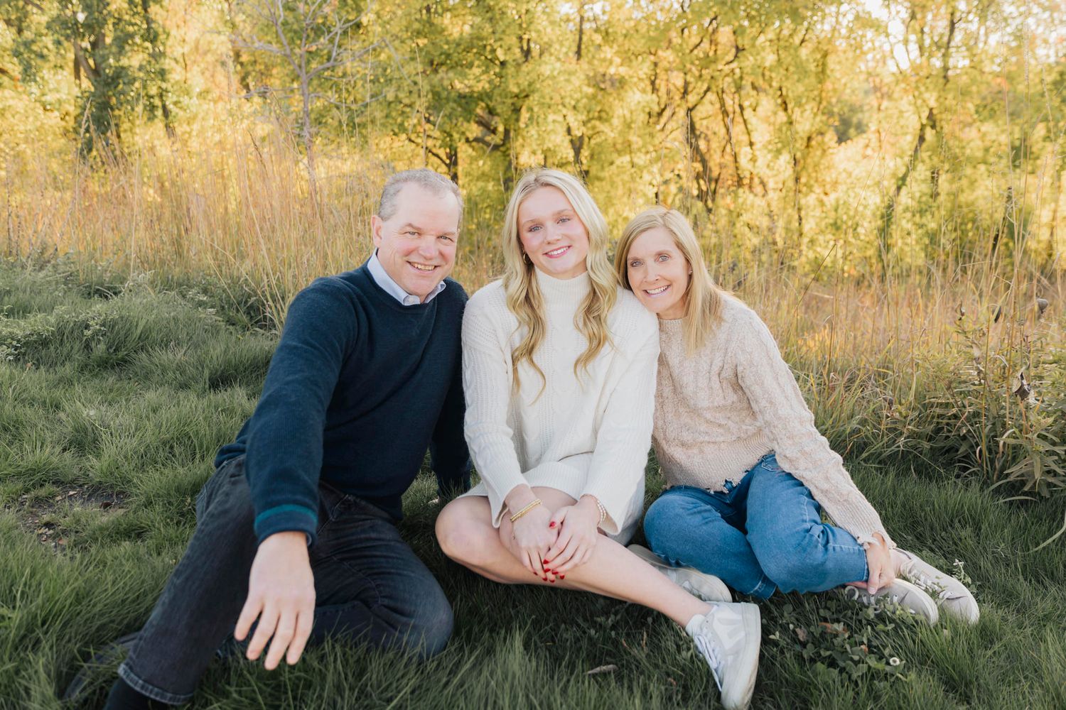 A family sits together on grass during golden hour in a natural outdoor setting.