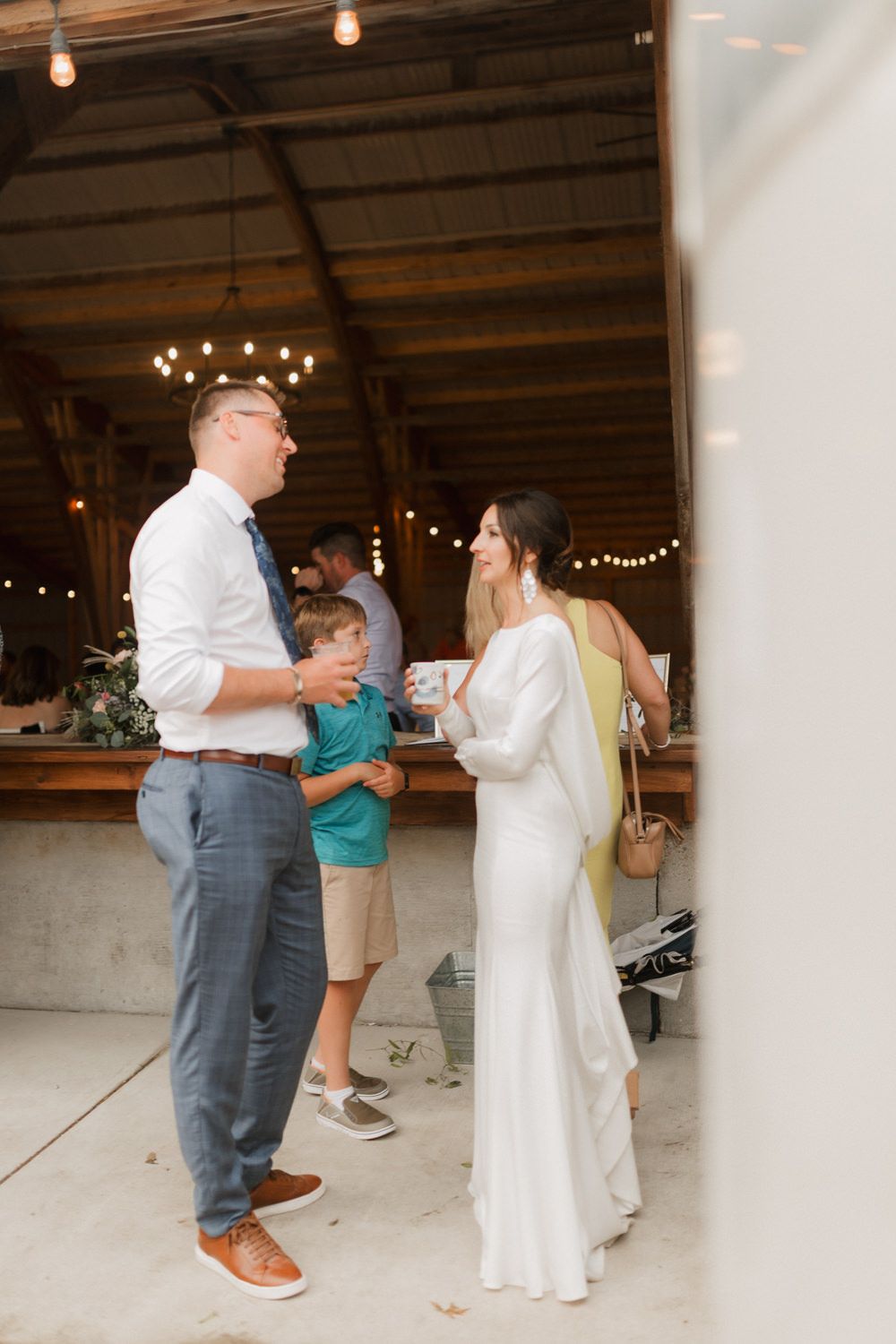 Wedding guests dance together in a rustic barn venue decorated with string lights.