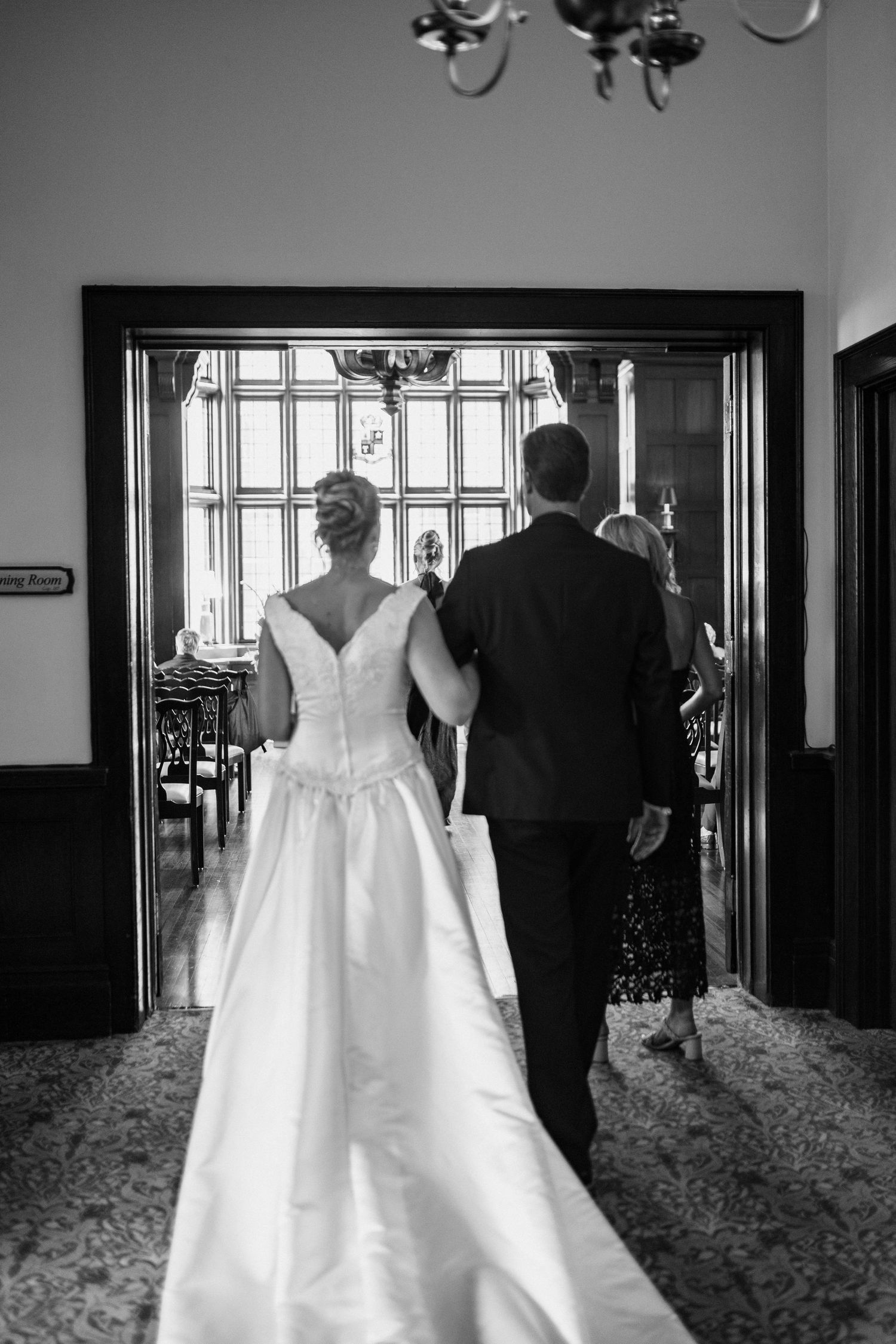 Black and white photo of bride and groom walking hand in hand through elegant doorway on wedding day.
