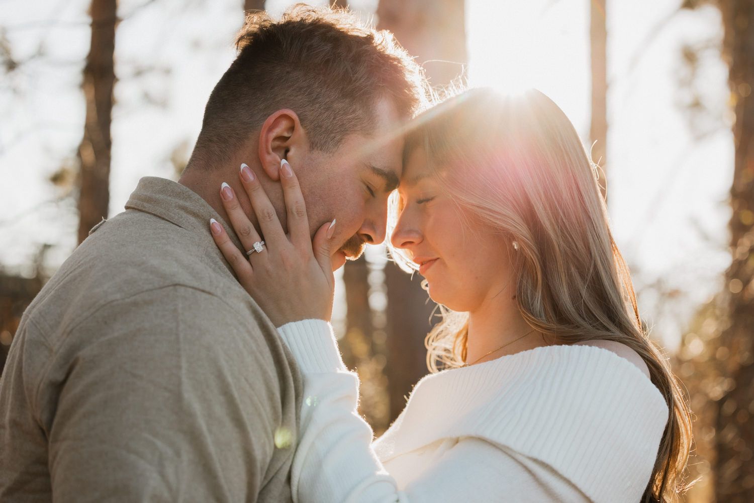 A couple shares an intimate moment backlit by golden sunlight in a field.