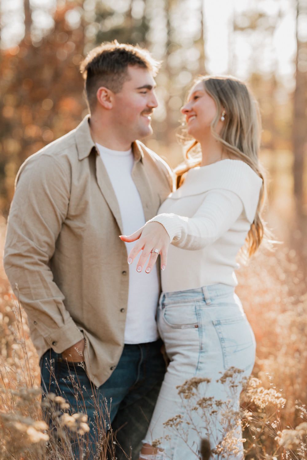 Romantic photoshoot in autumn field with couple in coordinated neutral colored outfits.
