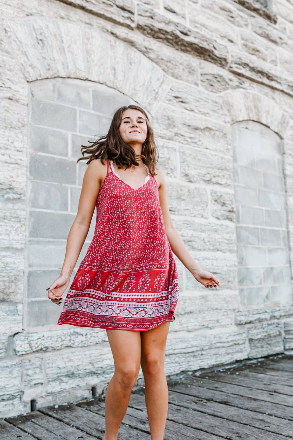 Woman in red floral dress twirling against stone wall backdrop.
