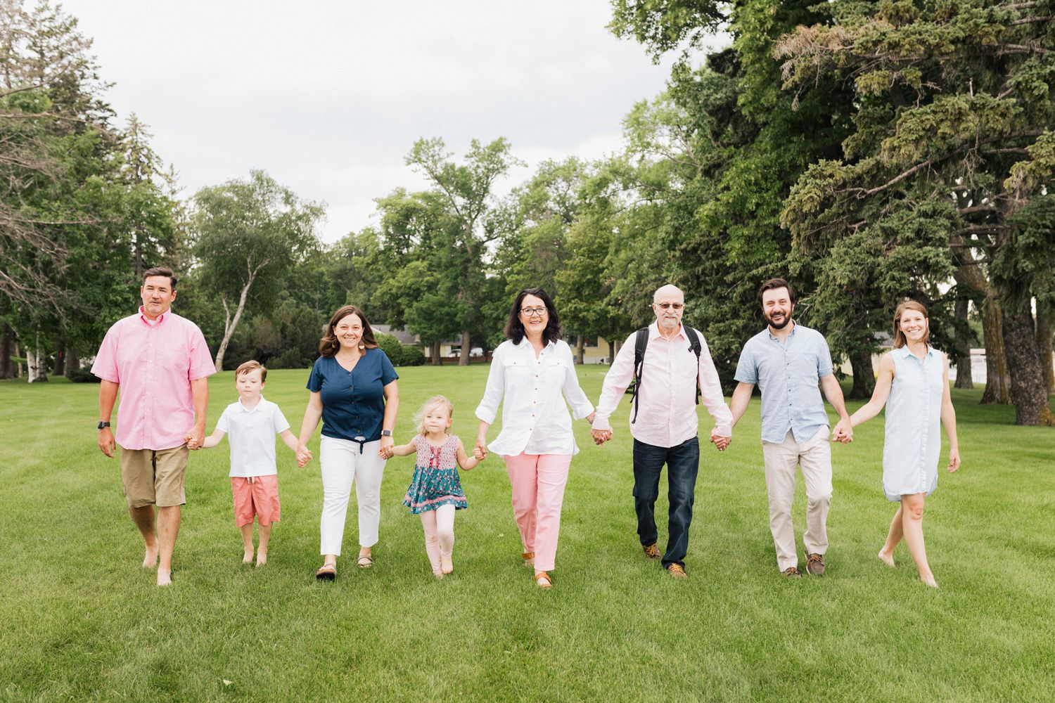 Extended family walking together in white and pink outfits across a grassy outdoor field.