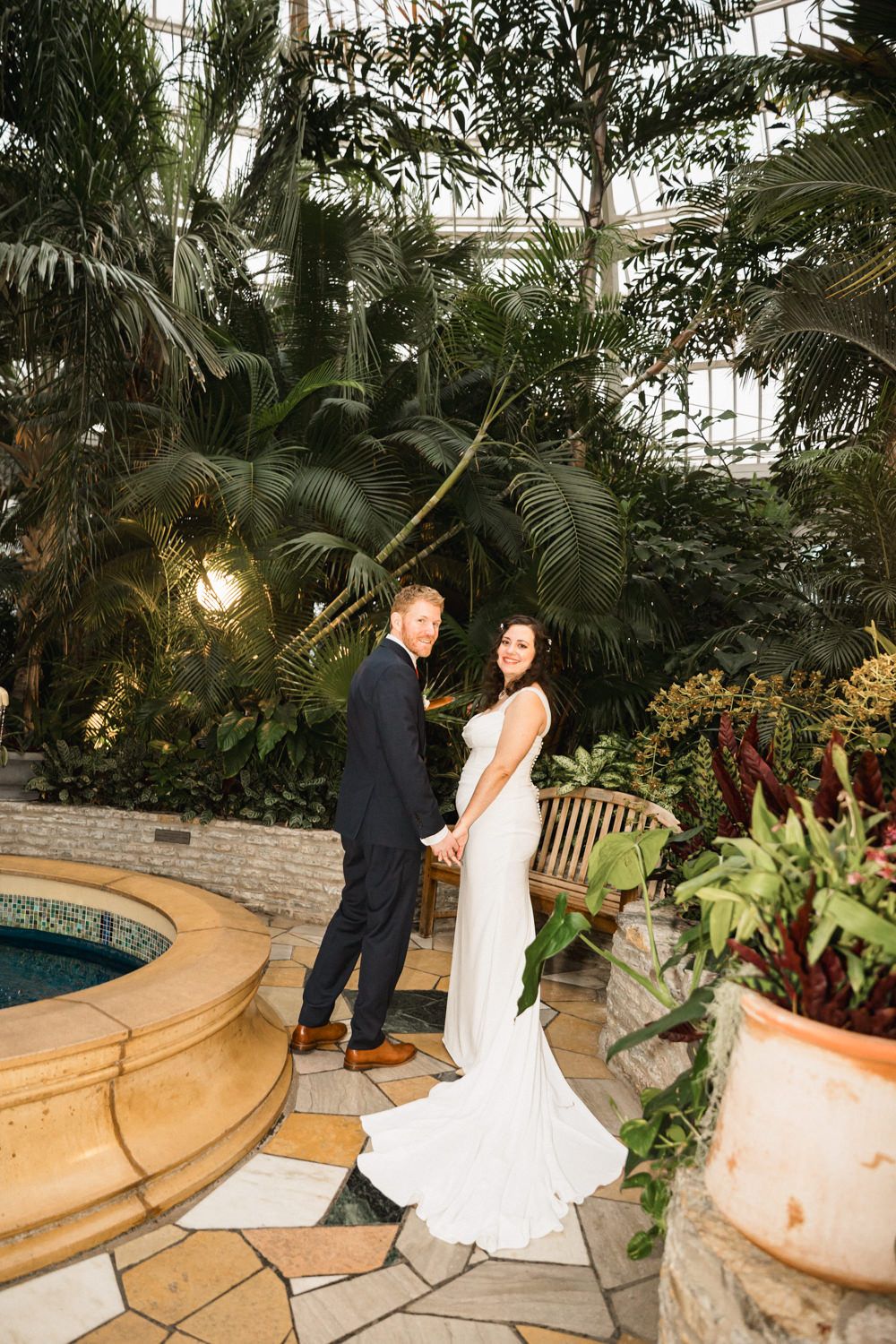 A romantic wedding photo in a lush indoor garden with tropical plants and mood lighting.