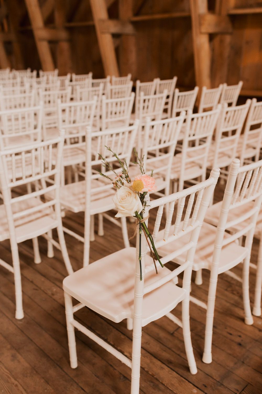 White wooden chairs arranged in rows with a delicate floral arrangement tied to one chair at a wedding ceremony venue.